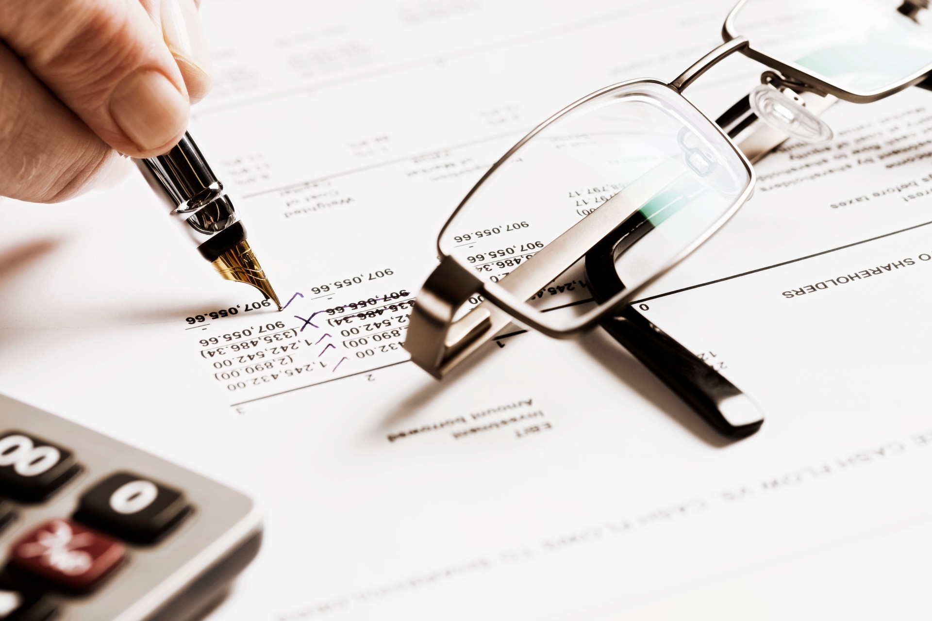 Man's hand checking figures on spreadsheet, with calculator and spectacles